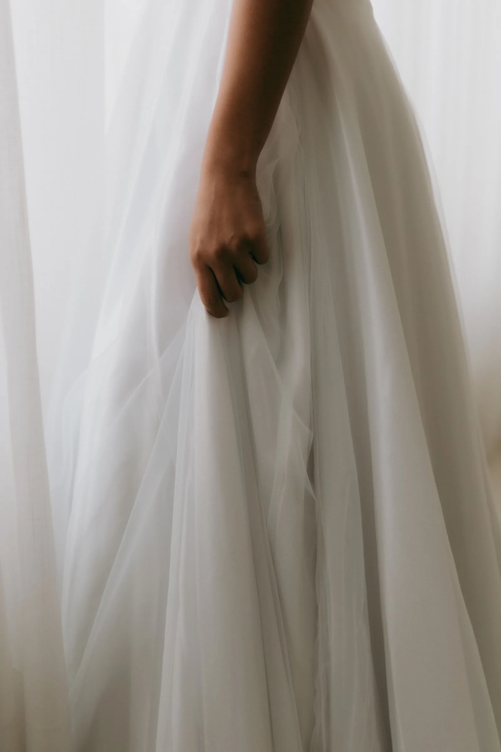 A hand holding the skirt of a white dress