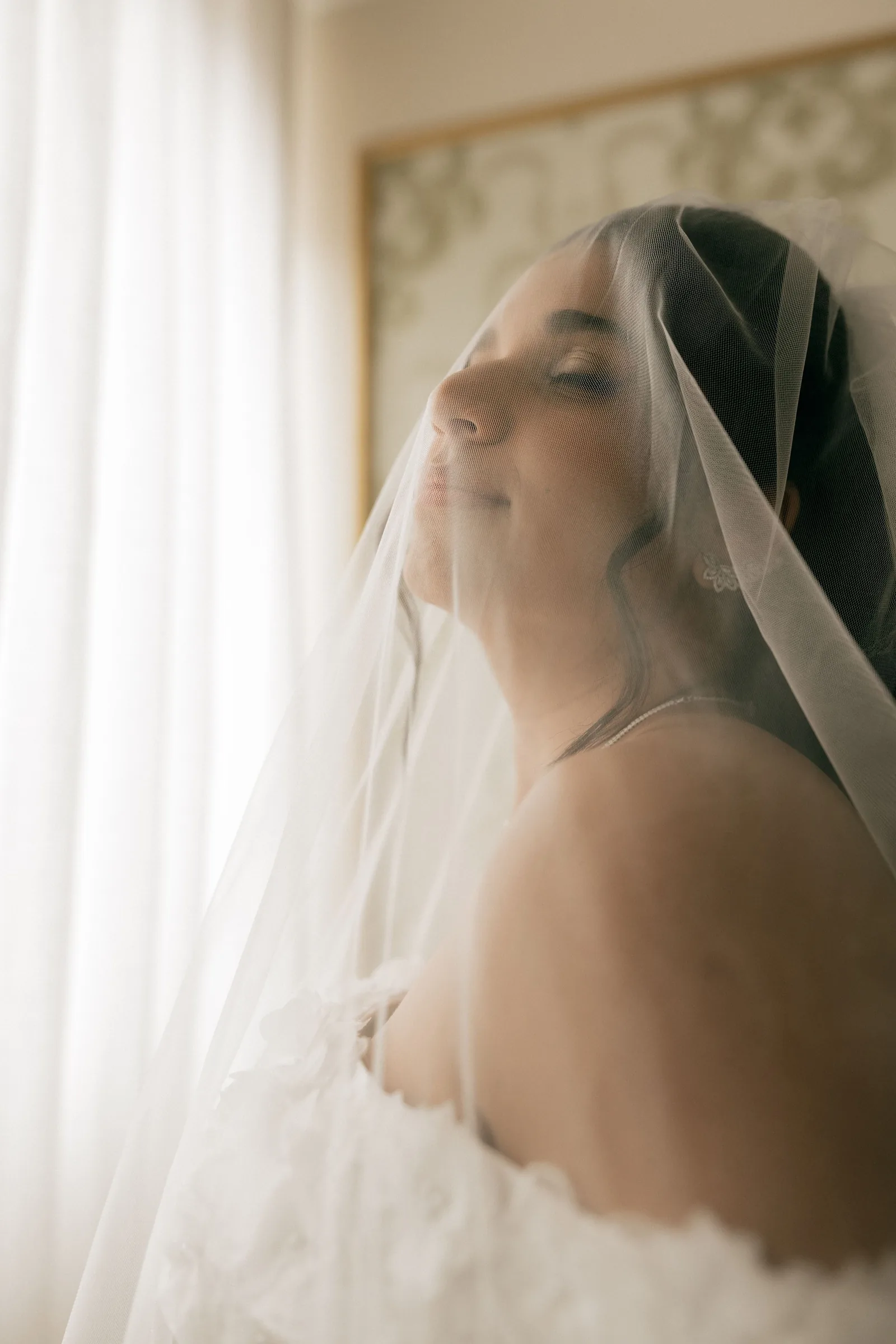 A bride under a long veil by a sunlit window